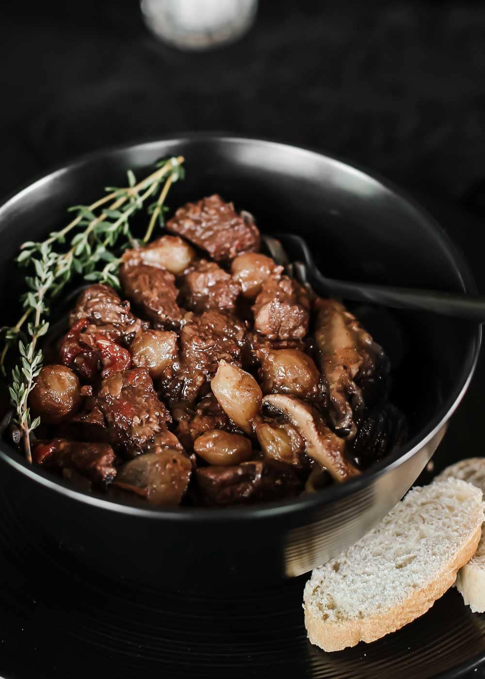 beef tips with onions and mushrooms in black bowl with bread on the side.