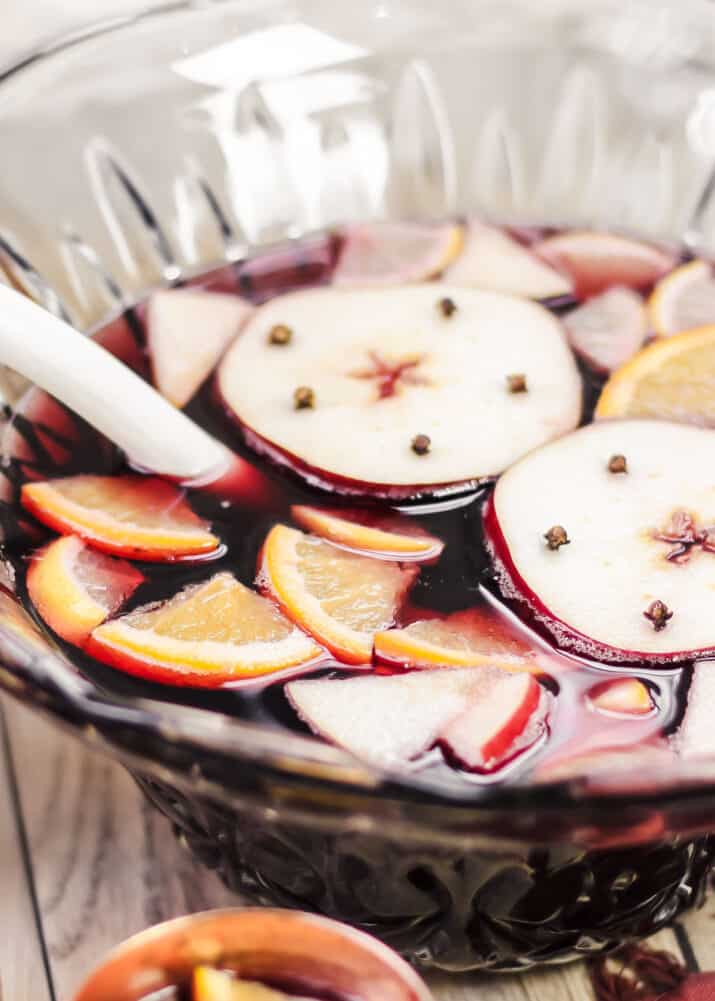 red sangria in punch bowl with apple and orange slices, and copper cups on the side.