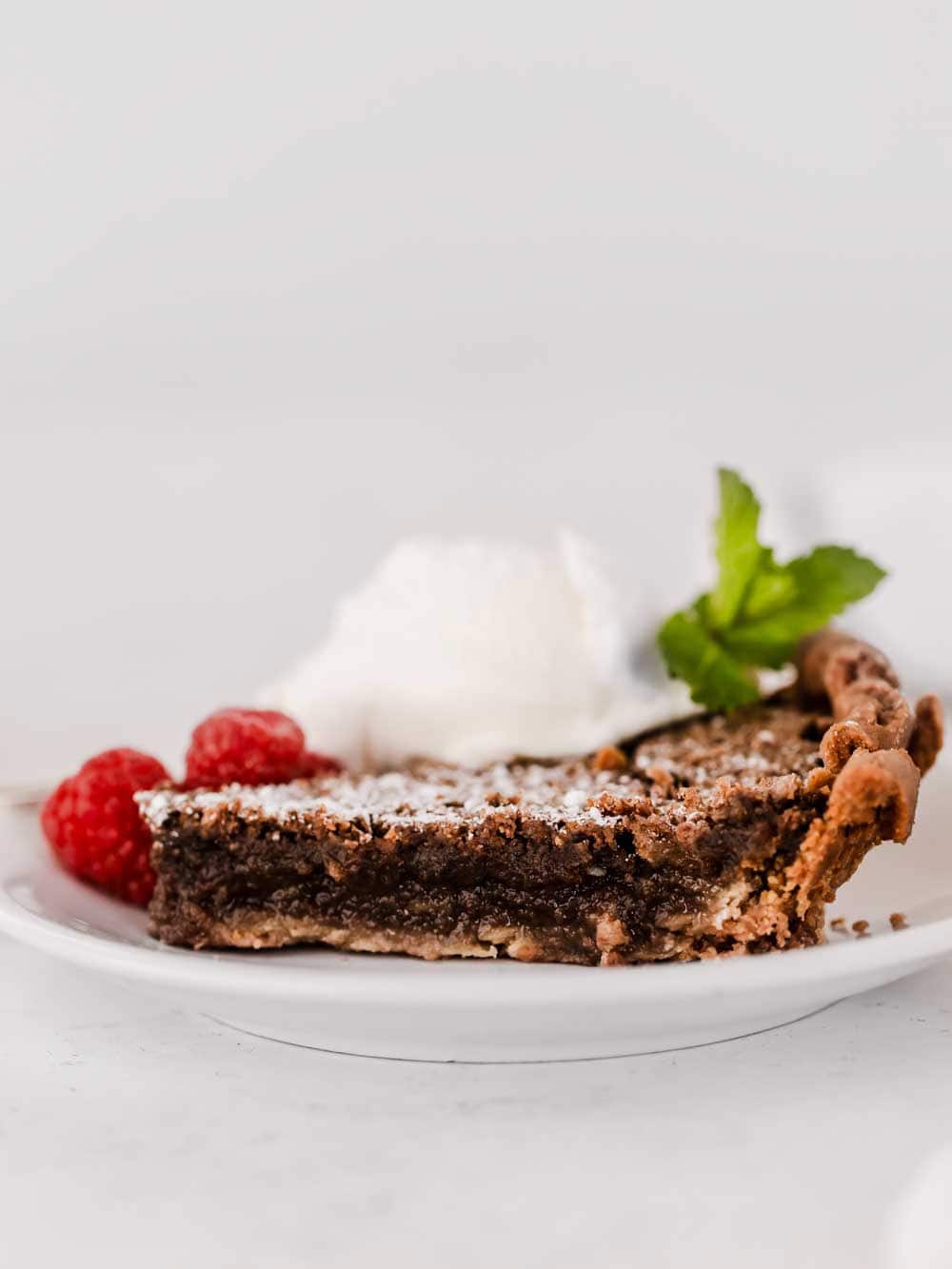 a slice of chocolate chess pie on white plate with ice cream scoop.