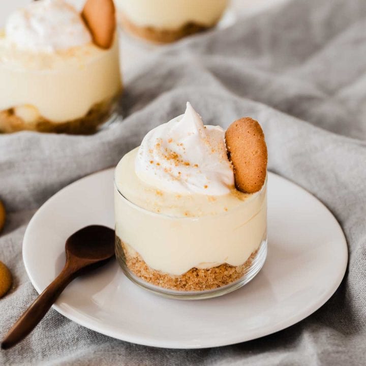 individual glass cup with banana pudding on white plate with spoon.