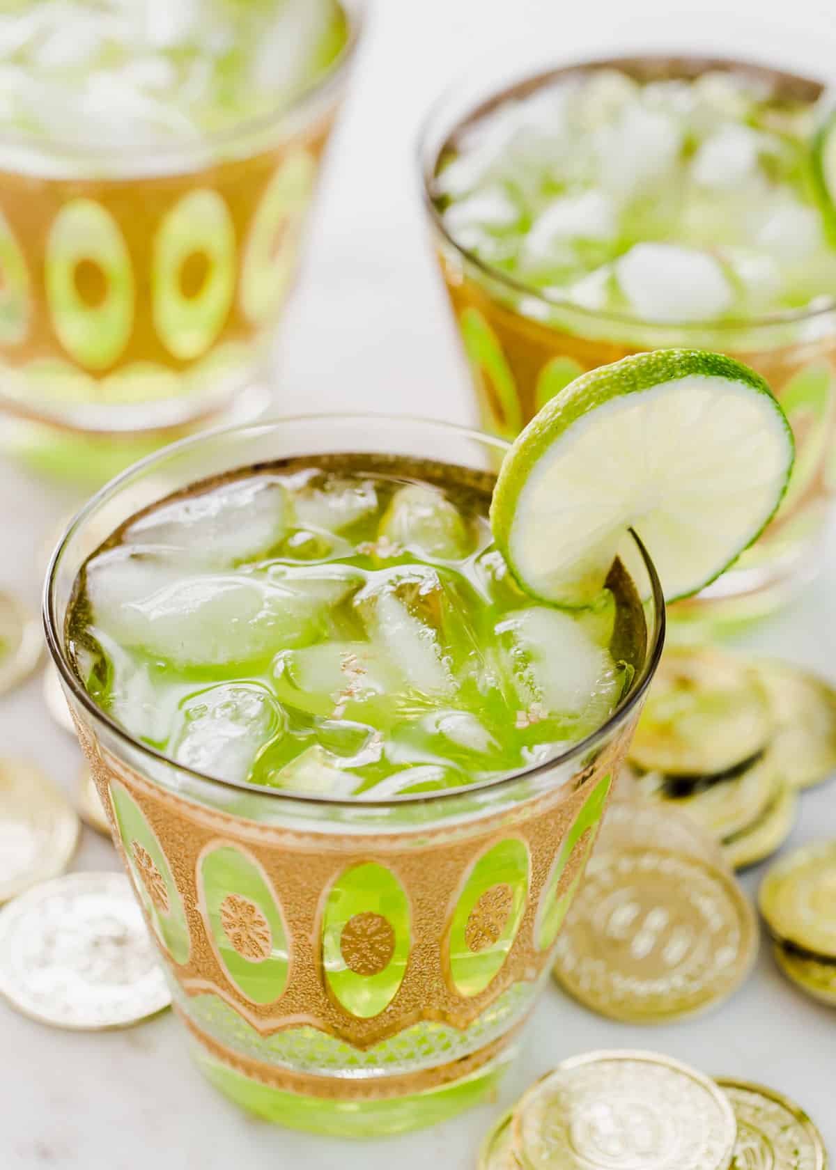 close up of green drink in vintage glass with lime slice garnish and gold flakes floating on top.
