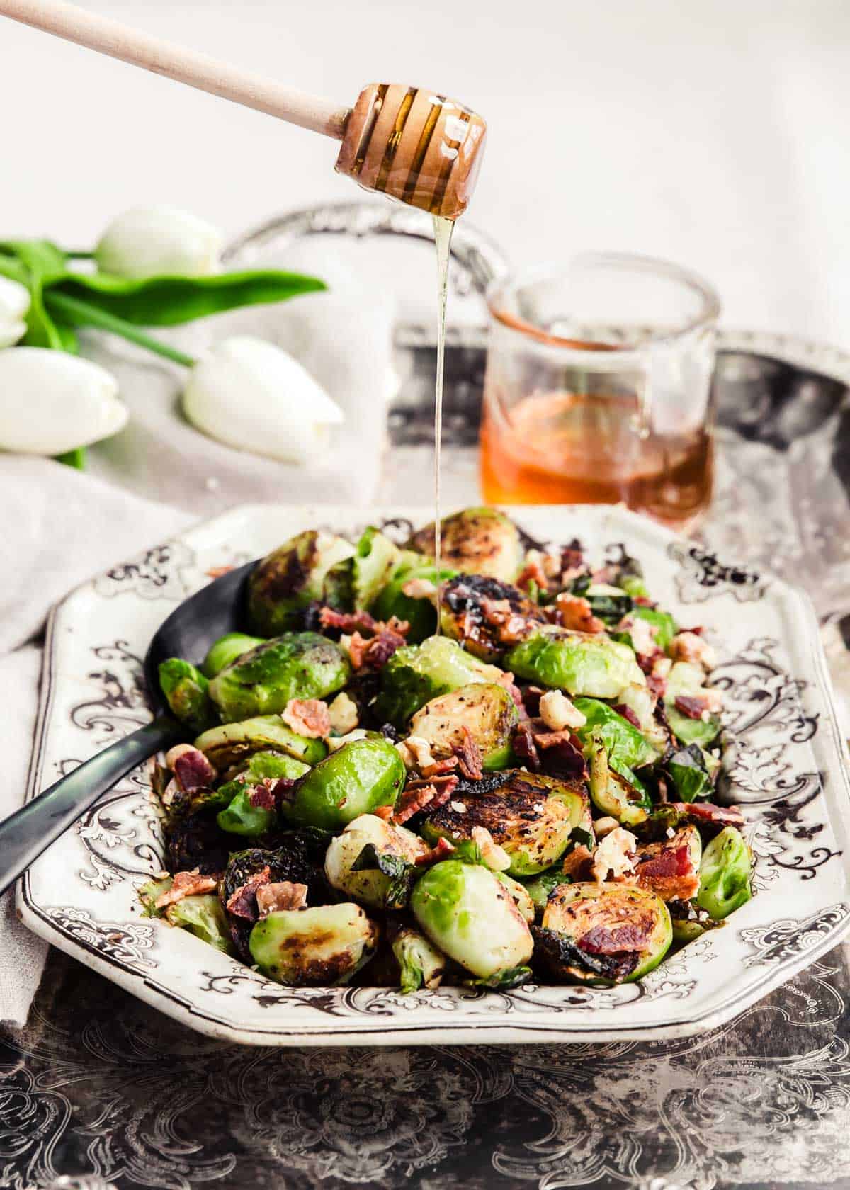 brussels sprouts with bacon and nuts served in vintage dish, with honey drizzling on top.