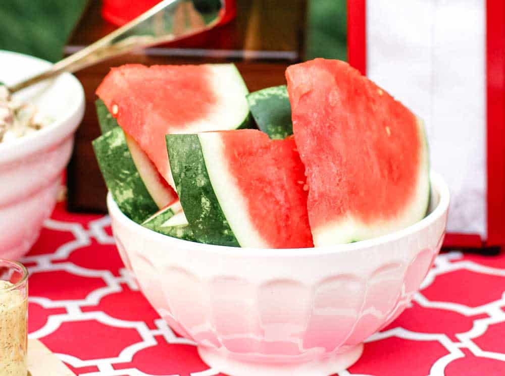 watermelon slices stacked in white bowl on outside table.