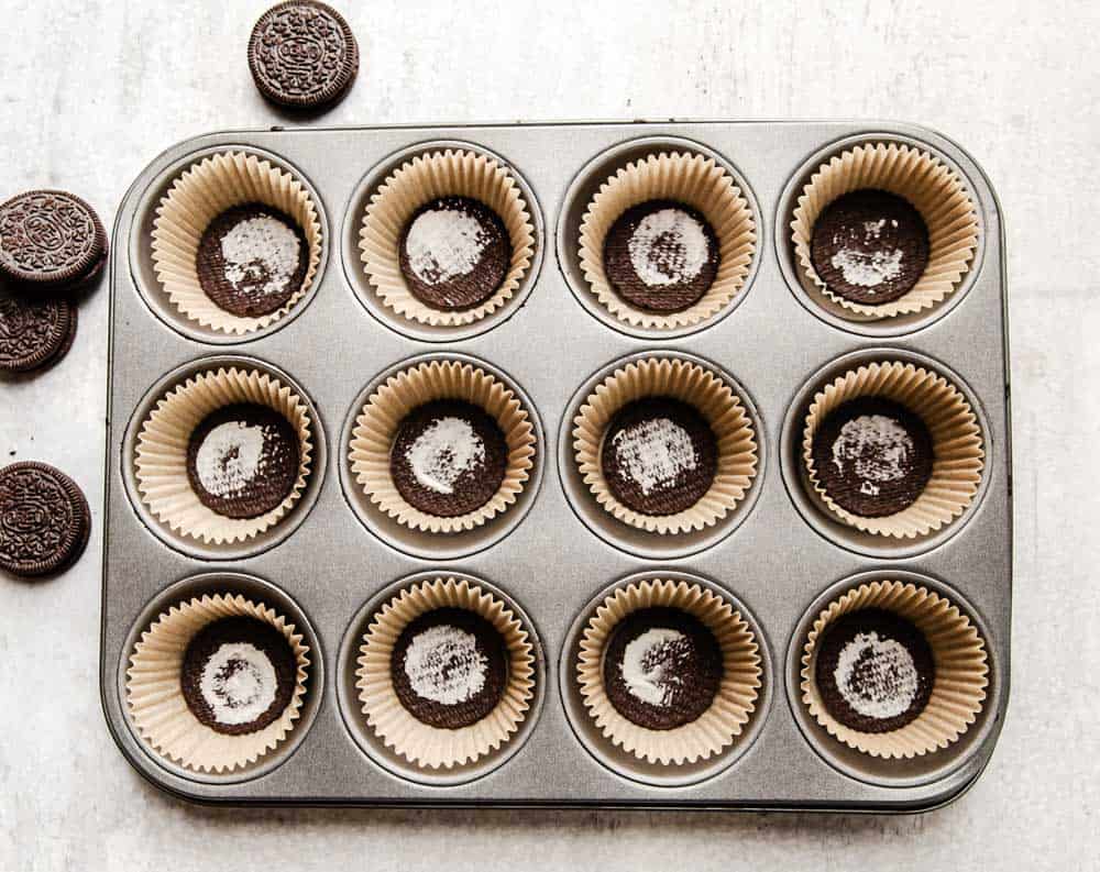 Oreo cookies in cupcake liners placed in muffin tins.