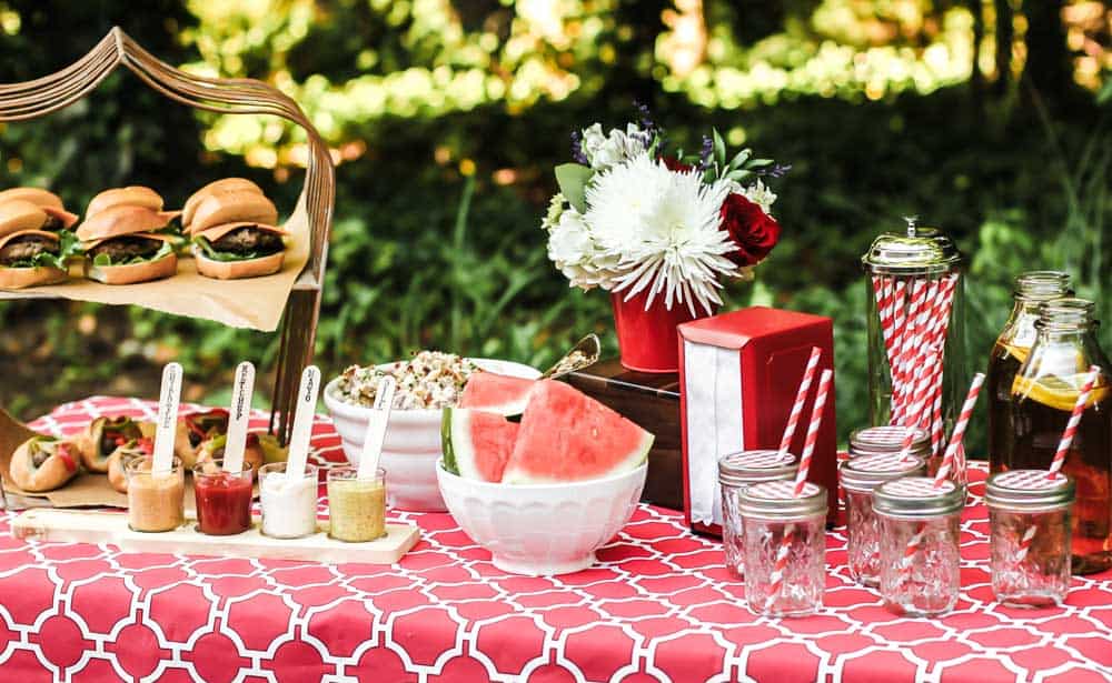 table setup outside with hamburgers, sausage dogs, condiments, and drinks.