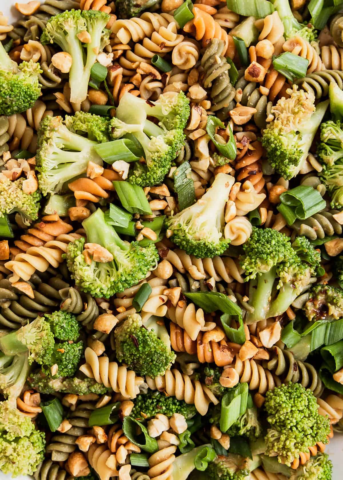 close up of broccoli and pasta salad with peanuts, scallions and red pepper flakes.