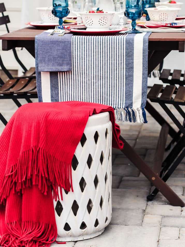 white garden stool draped with red throw, at end of outdoor dining table.