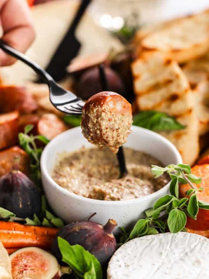 sausage medallion dipped into grainy mustard bowl.
