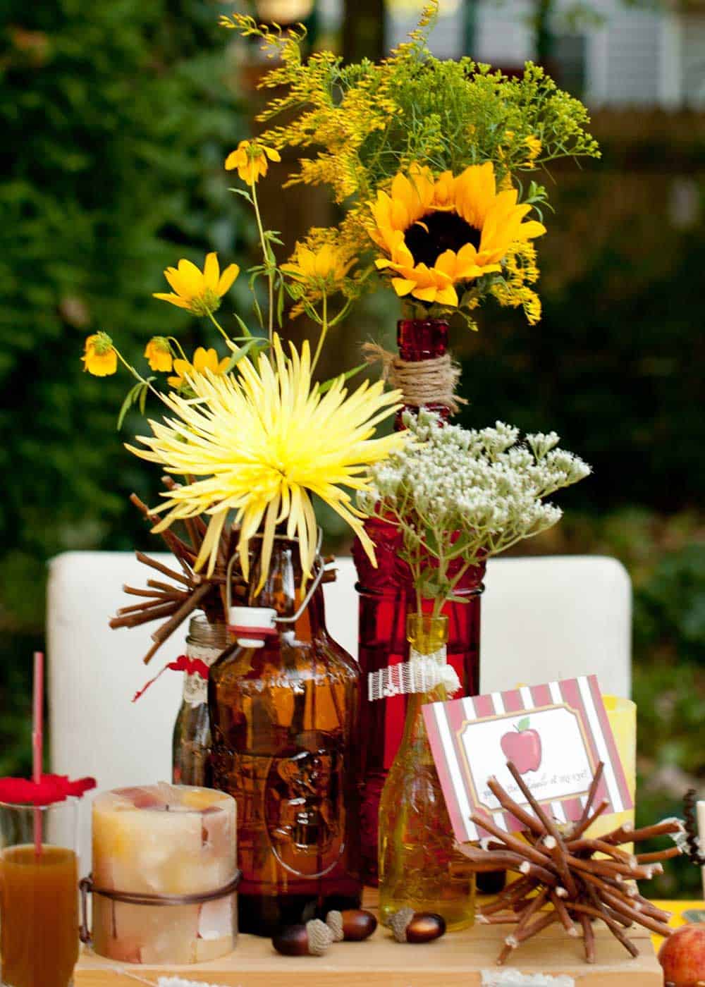 dinner table centerpiece of wildflowers in fall toned bottles, in outdoor setting.