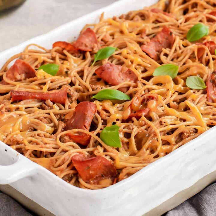 cheesy spaghetti with pepperoni and basil on top, in white casserole dish.
