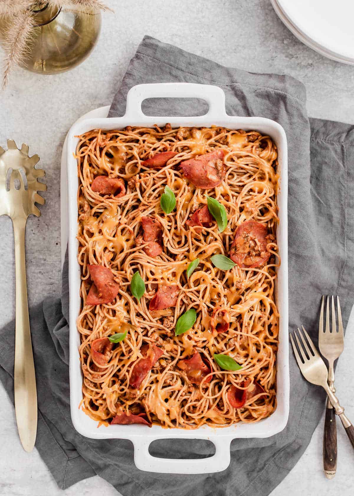 cheesy spaghetti with pepperoni and basil on top, in white casserole dish, overhead view.