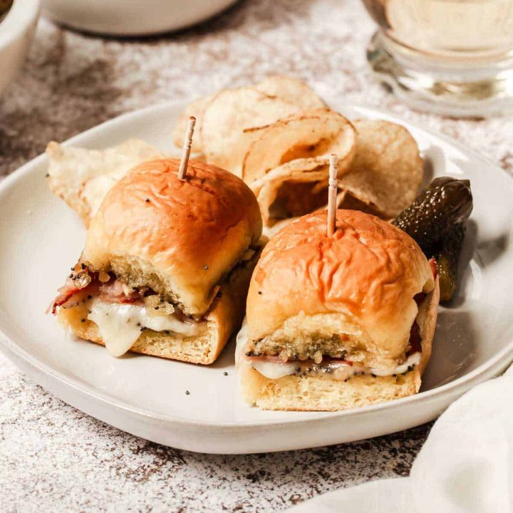 Baked ham and Swiss sliders on small plate with chips and pickles.