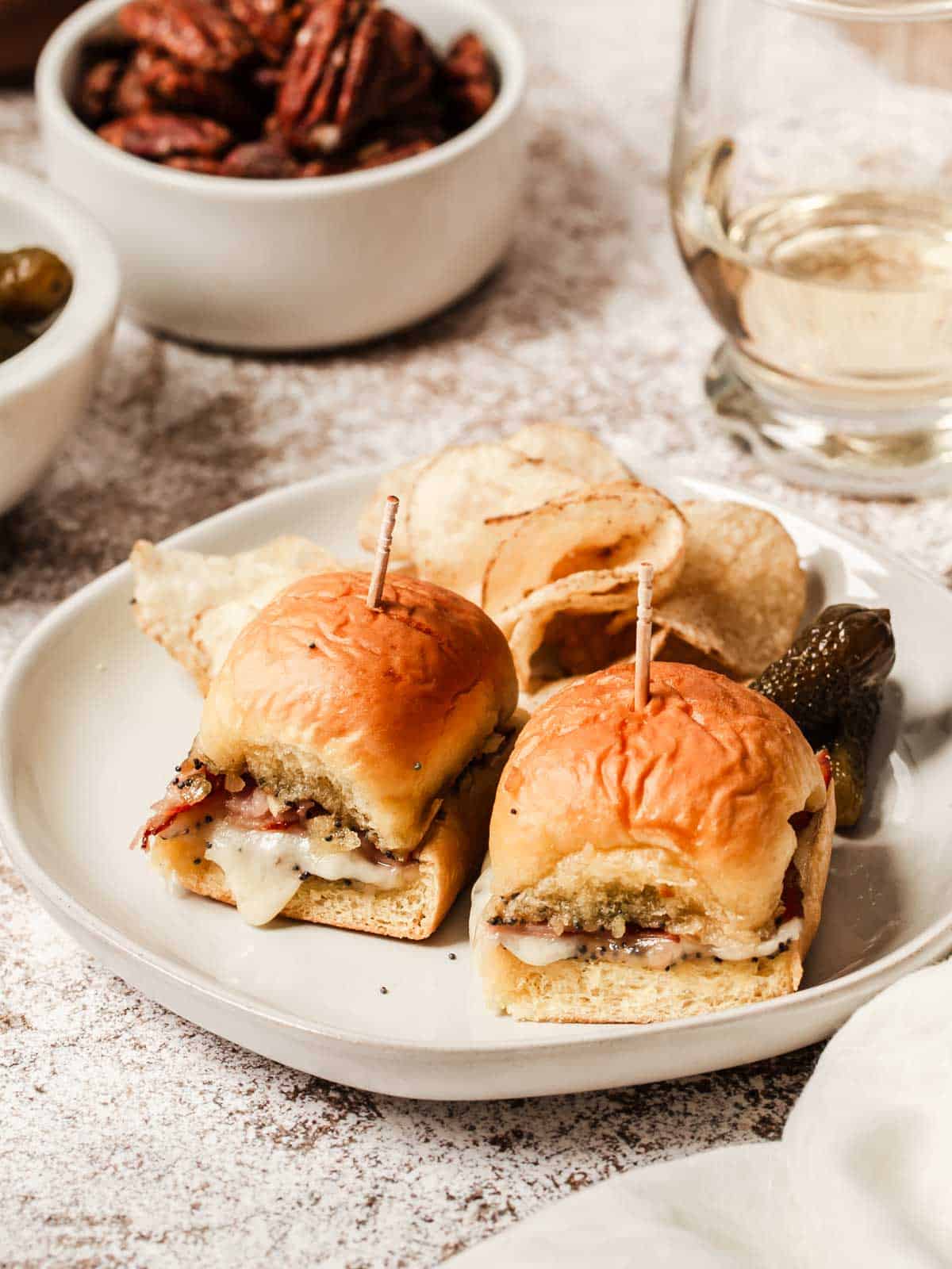 Baked ham and Swiss sliders on small plate with chips and pickles.