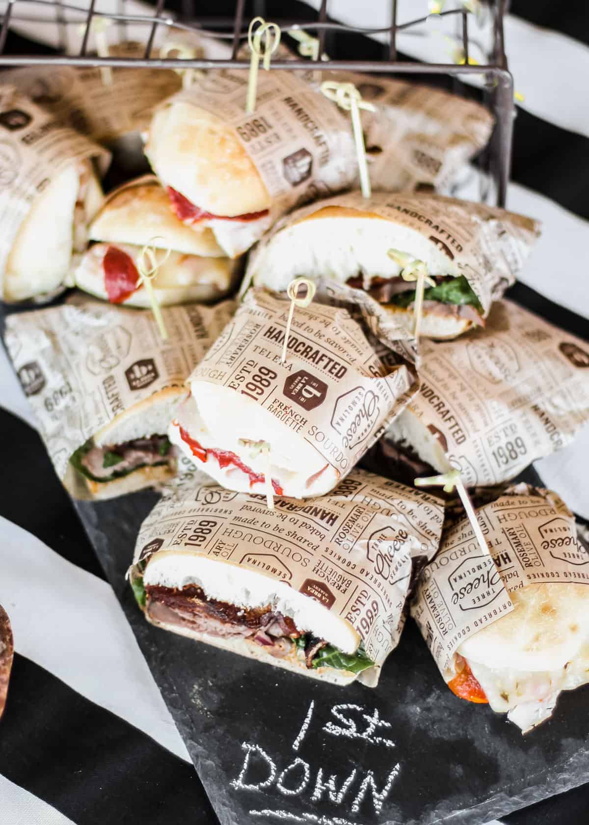 sandwiches wrapped in bakery paper, piled on party table.