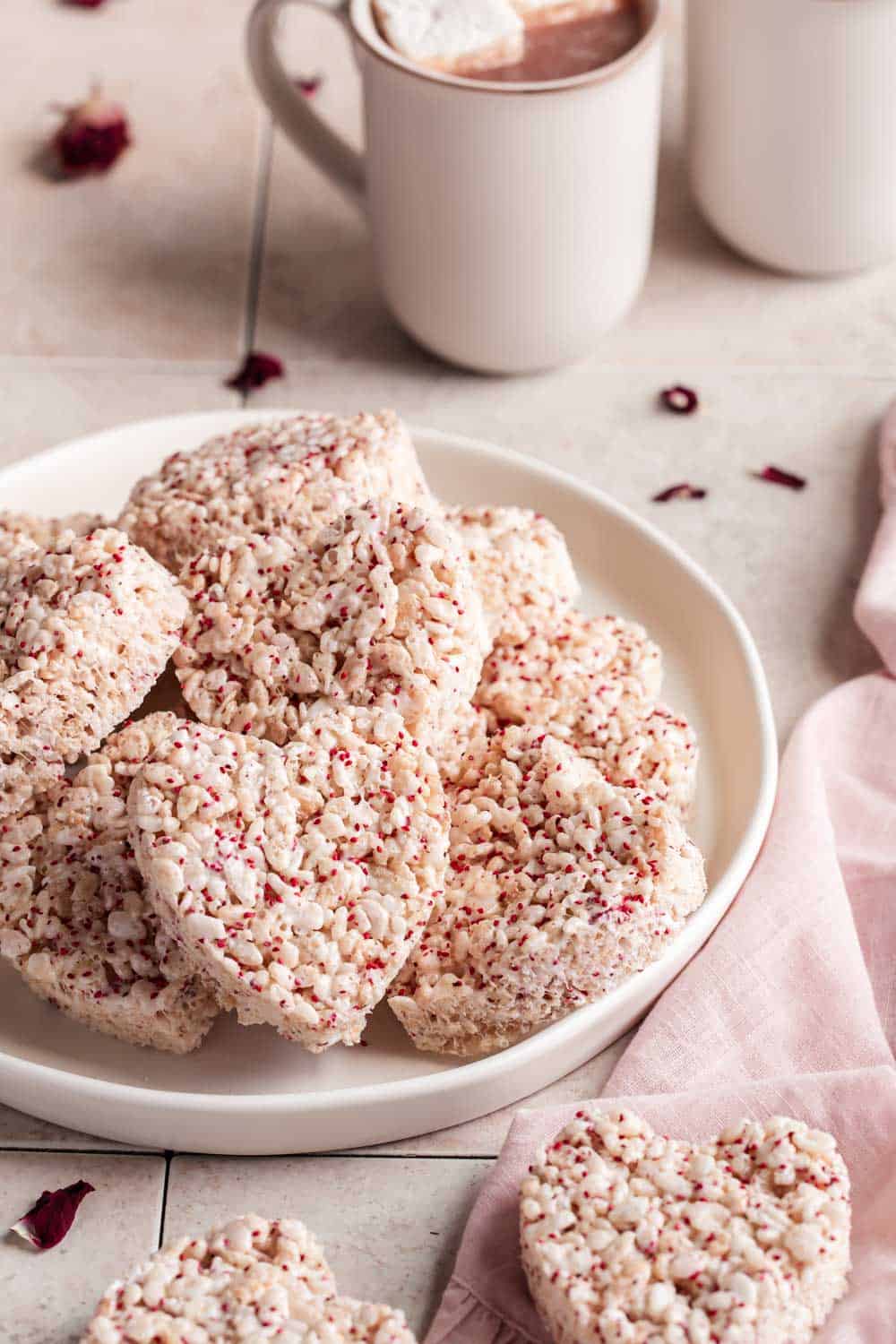 heart shaped rice krispies treats on a plate with hot chocolate mugs to the side.