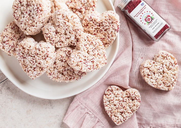 puffed cereal treats on plate with jar of red seeds, on pink napkin