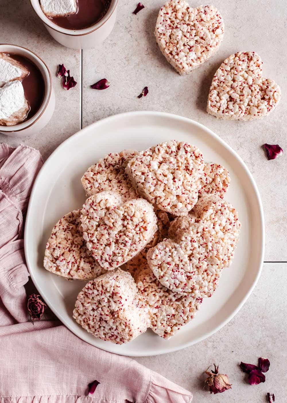 heart shaped rice krispies treats on a plate with hot chocolate mugs to the side.