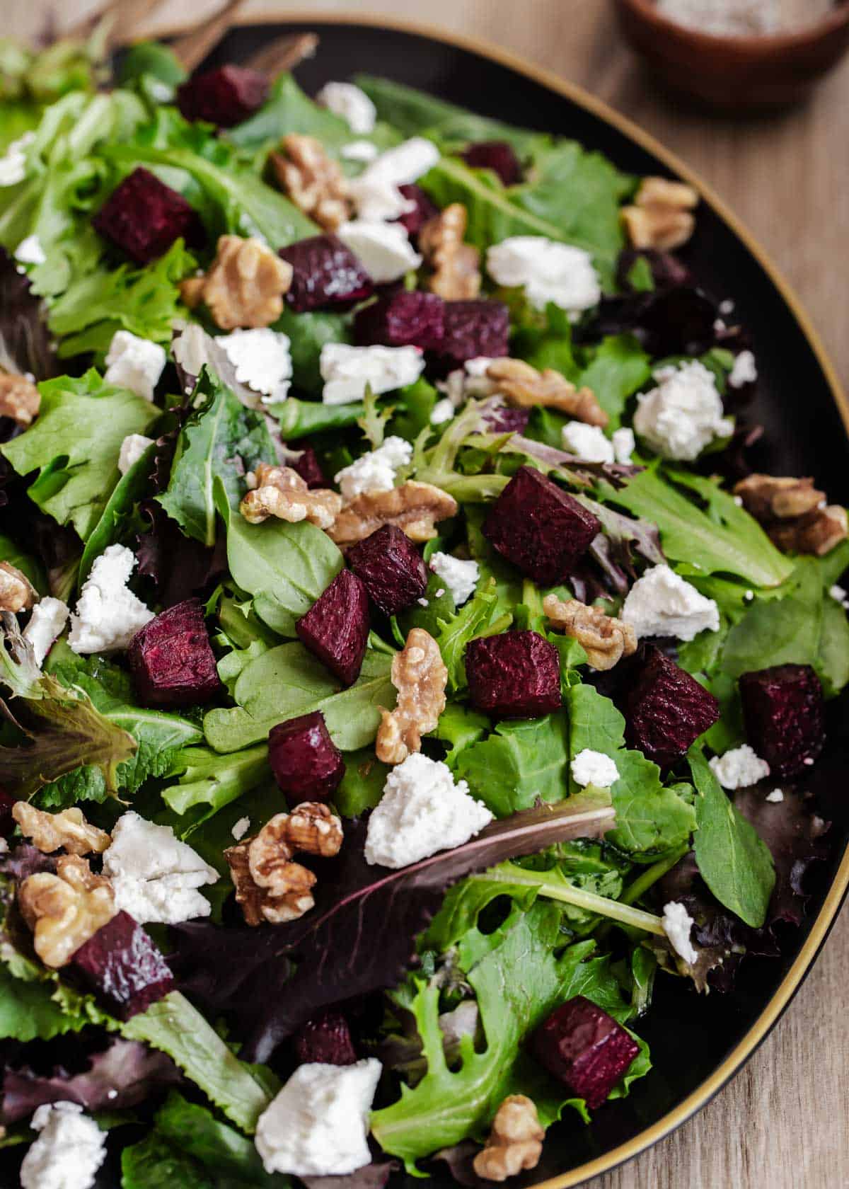 green salad with roasted beets and goat cheese on black platter.