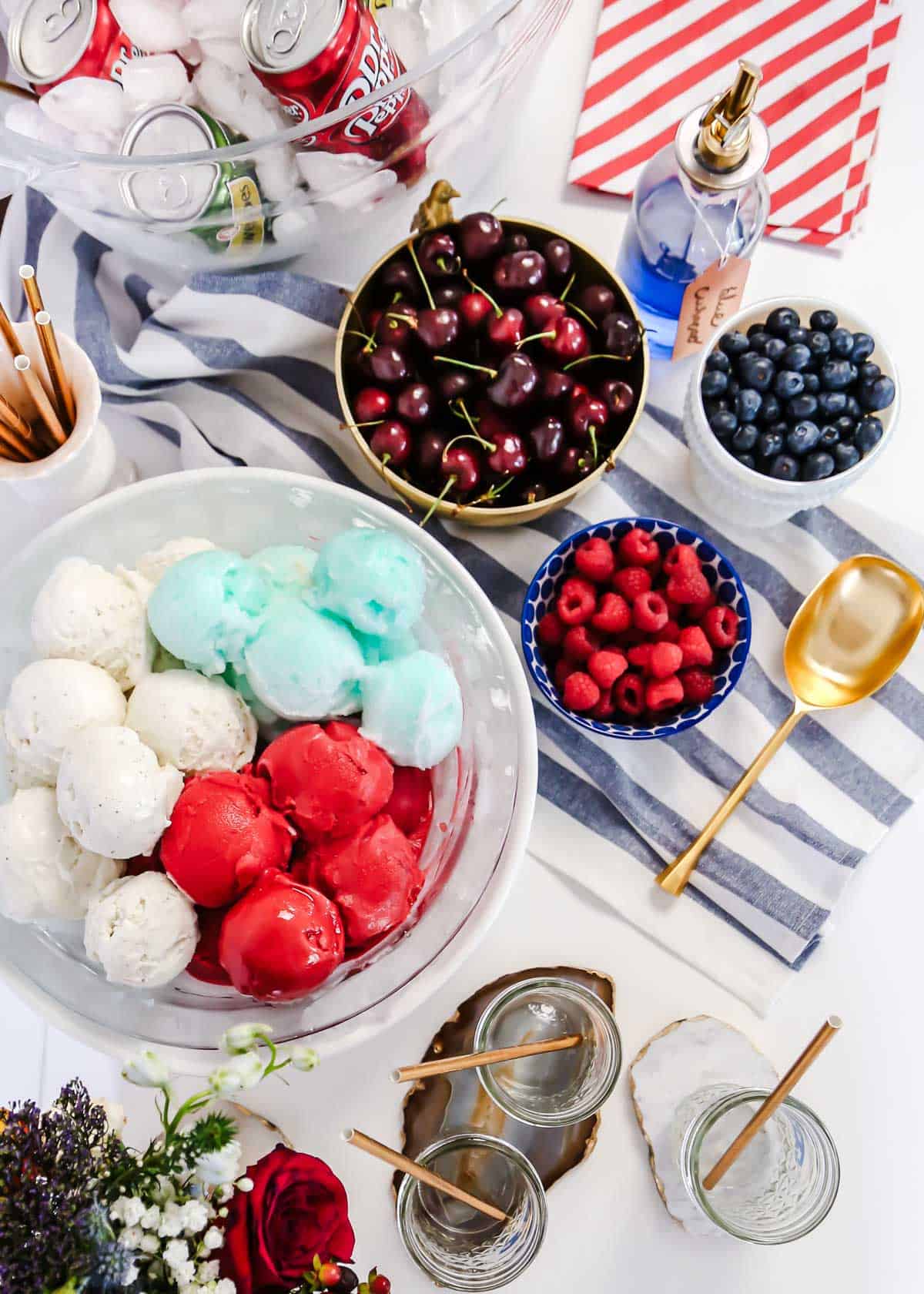 red, white and blue ice cream scoops in bowl surrounded by cherries, raspberries and blueberries.