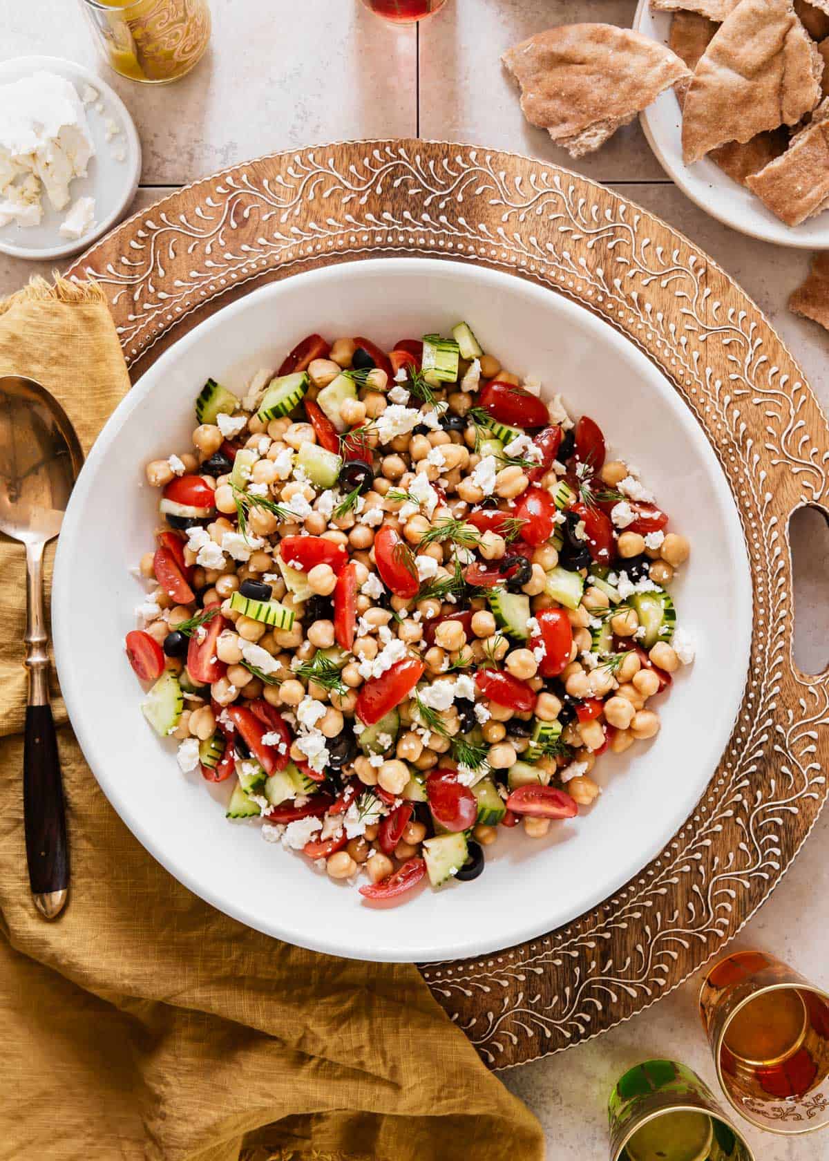 large white bowl with chickpeas, tomatoes, black olives, cucumber, and feta cheese.
