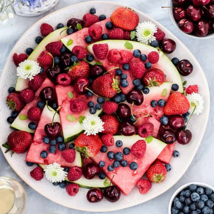 round platter with a mix of fresh berries and watermelon slices, on blue table with overhead view.