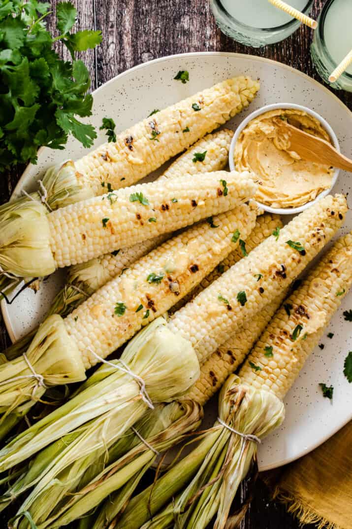 platter of grilled corn on the cob with flavored butter in small bowl