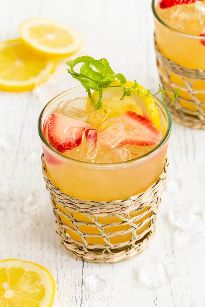 glass of orange drink with sliced strawberries floating inside.