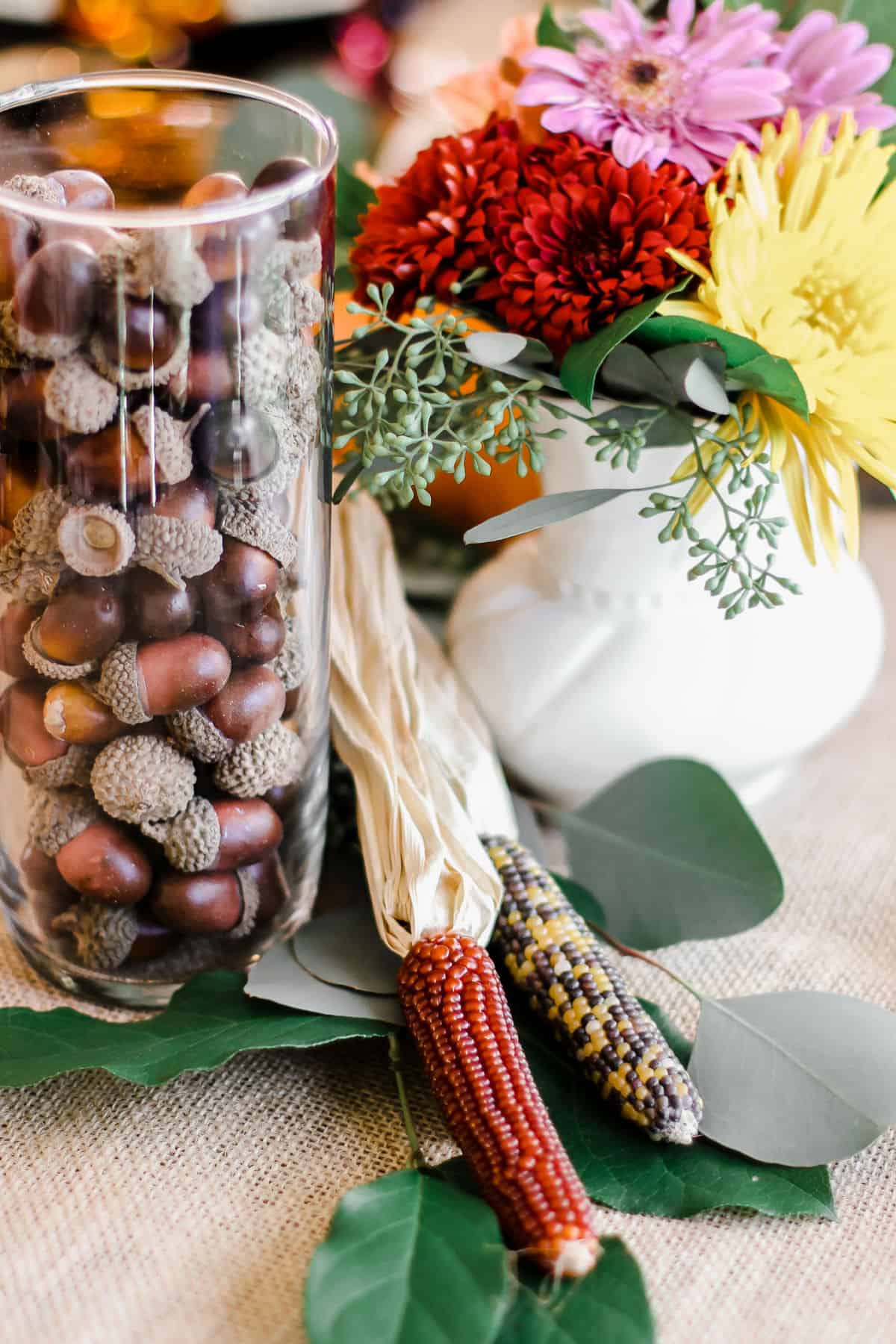 Thanksgiving table decoration of vase filled with acorns, baby corn, and flowers