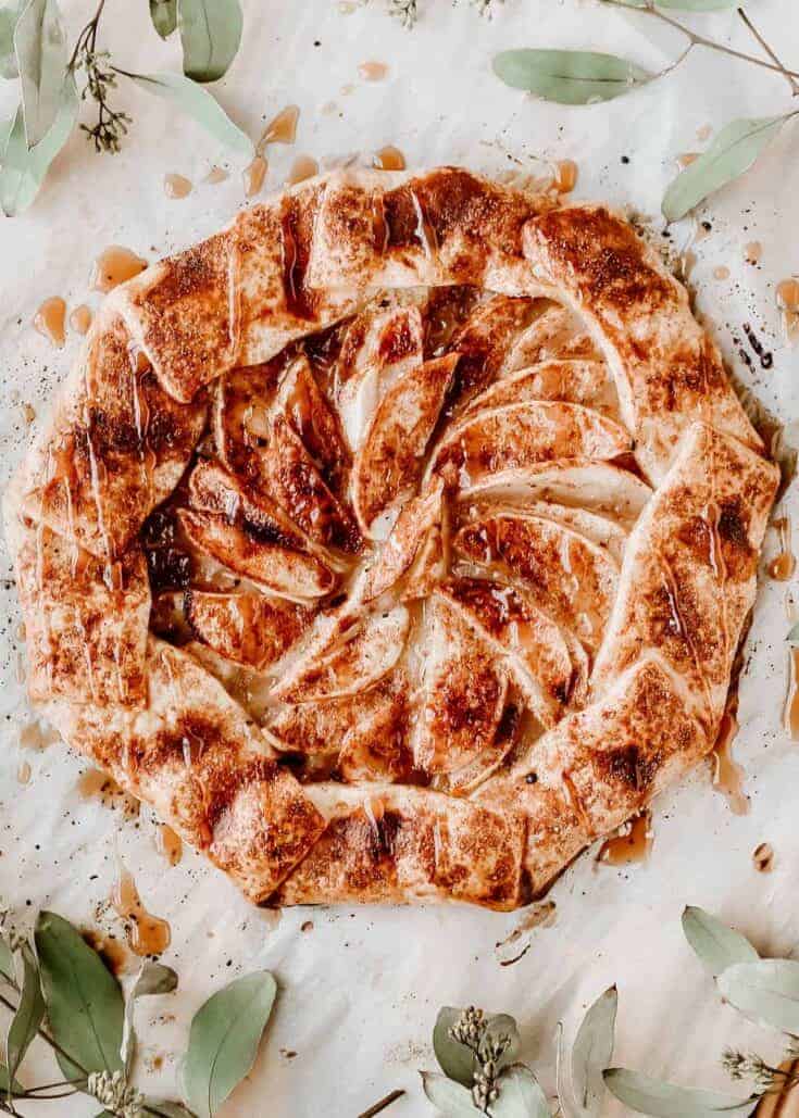 rustic apple galette on parchment paper surrounded by leaves, overhead.