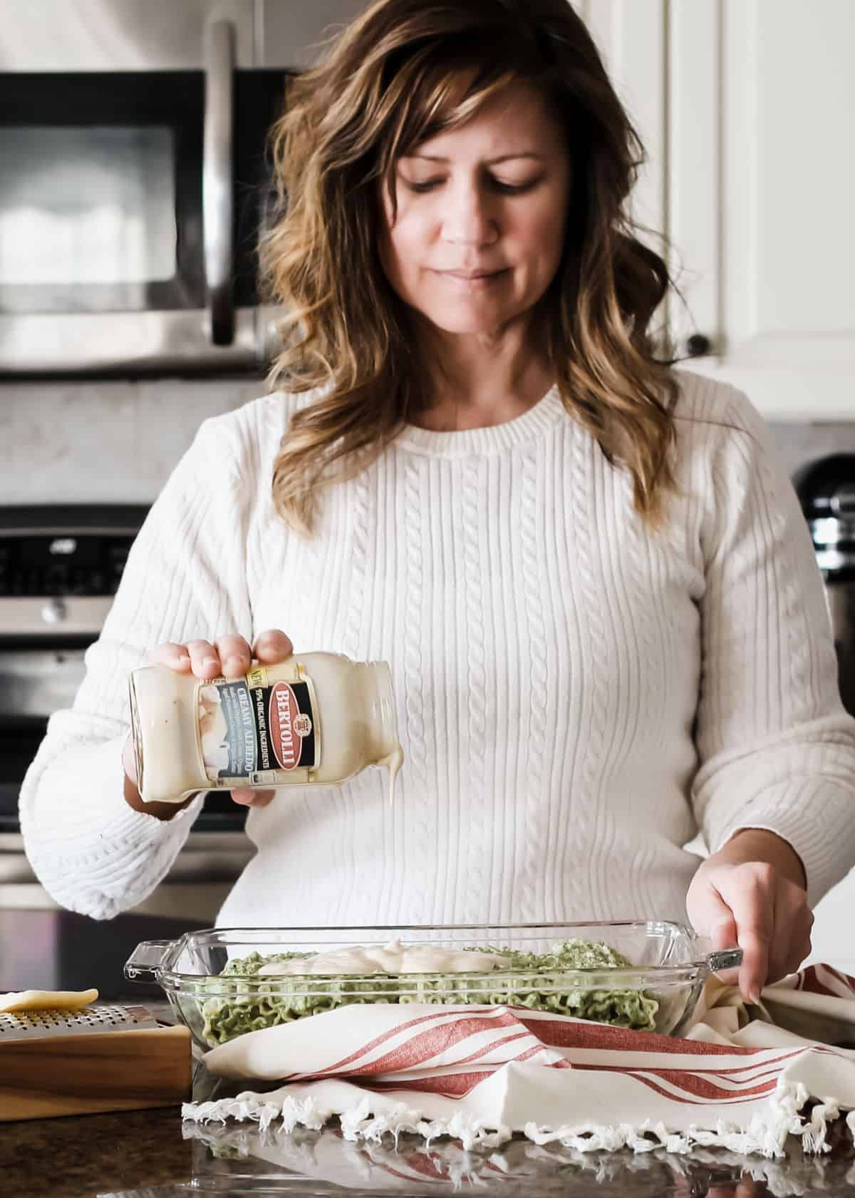 lady in white sweater in kitchen making a casserole.