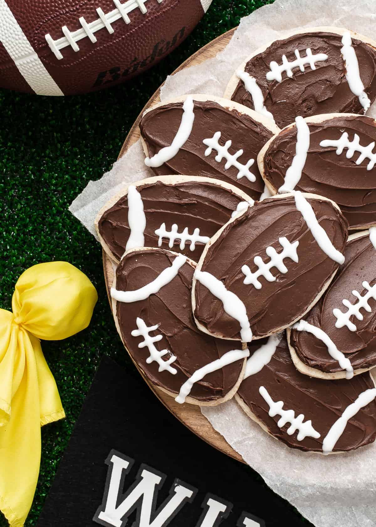 football shaped and decorated cookies on round tray with football paraphernalia surrounding.