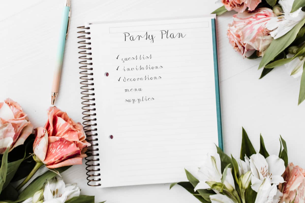 party planning notebook surrounded by flowers, on white table.