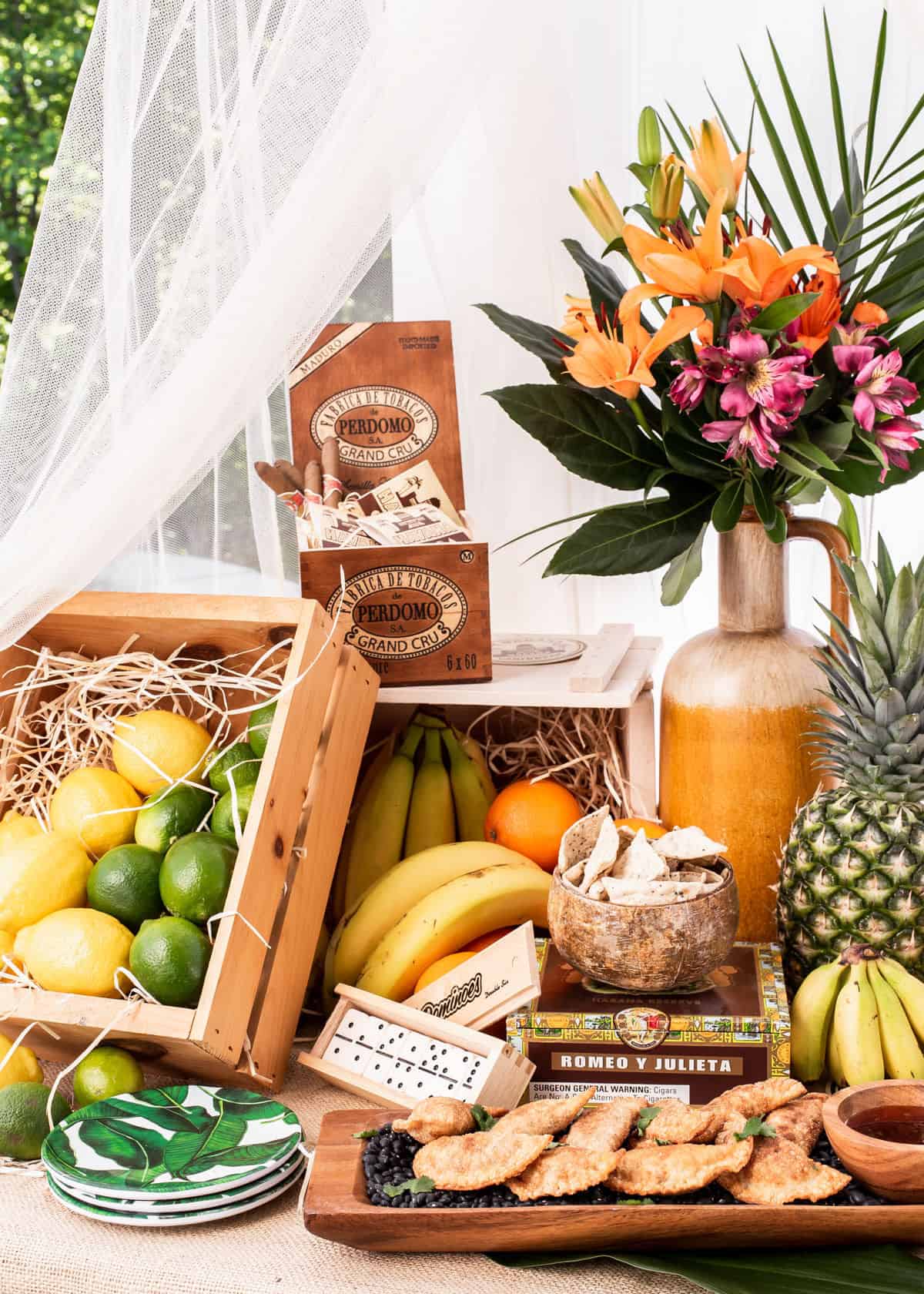 tropical themed party decorations set up outside, with wood crates, fruit and tropical flowers.