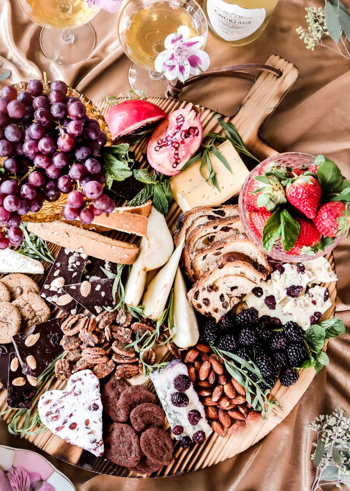 round wood board filled with cheese chocolate fruit nuts and sweets.