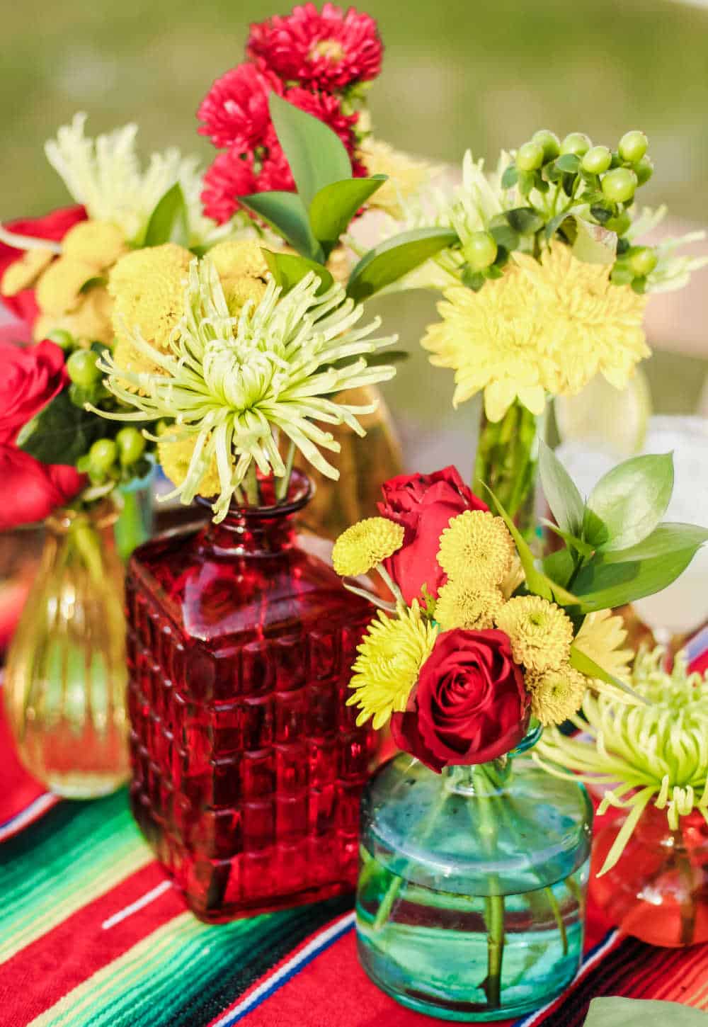 colorful arrangement of flowers in small glass vases on Mexican serape.