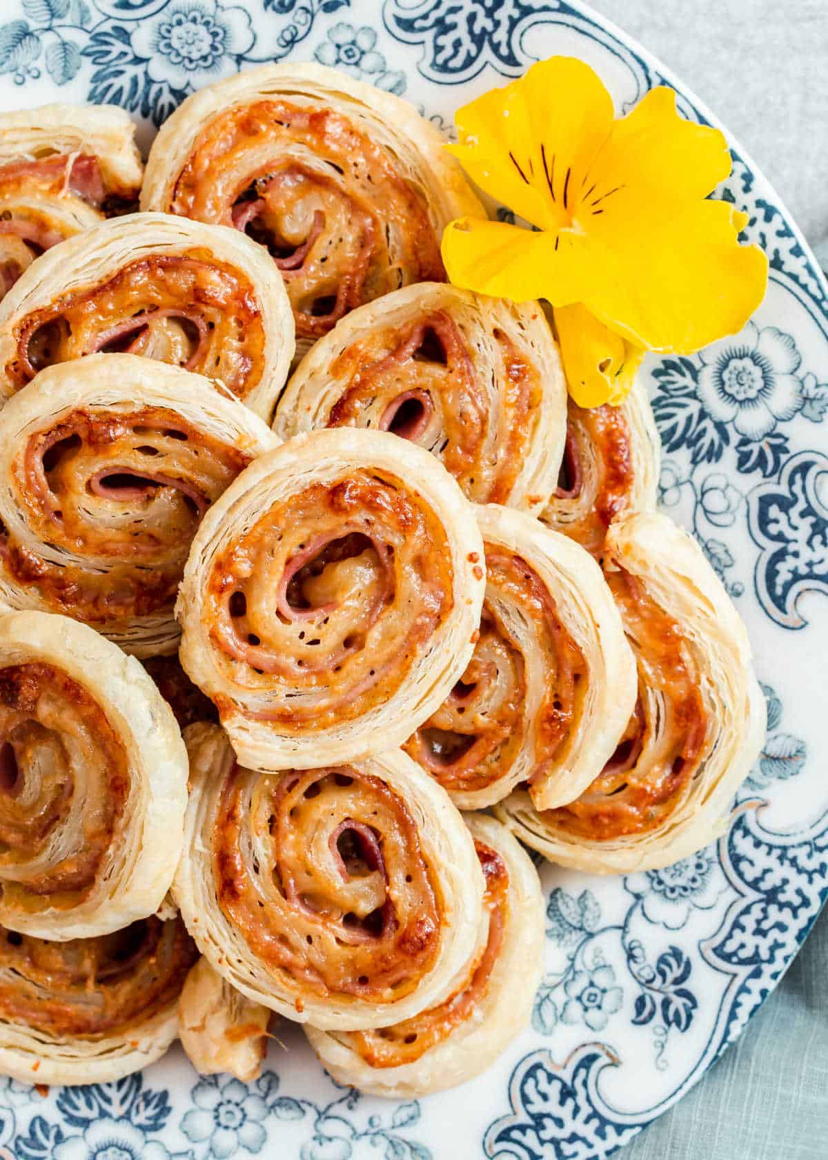 ham and cheese puff pastry pinwheels on blue floral plate.