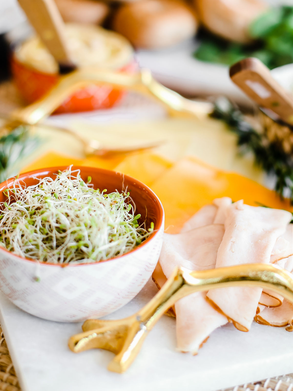 marble board with deli meat and cheese and sprouts in a bowl.