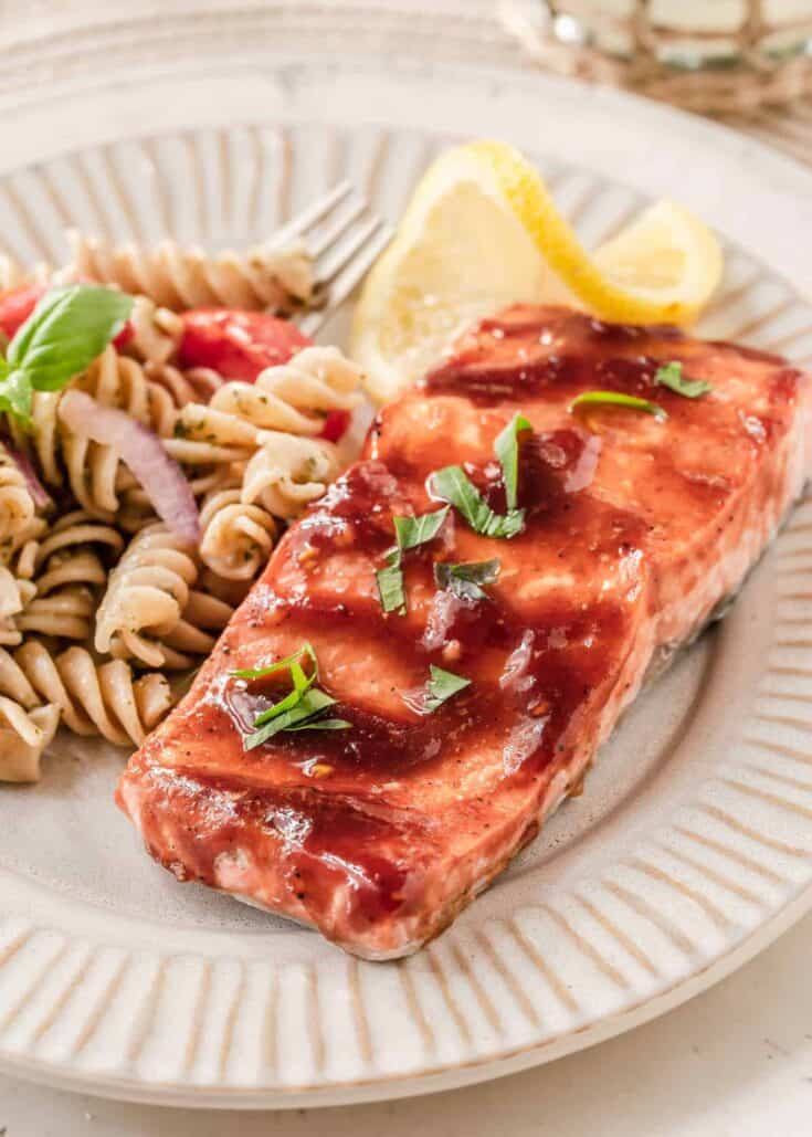 salmon brushed with bbq sauce on plate with pasta salad.