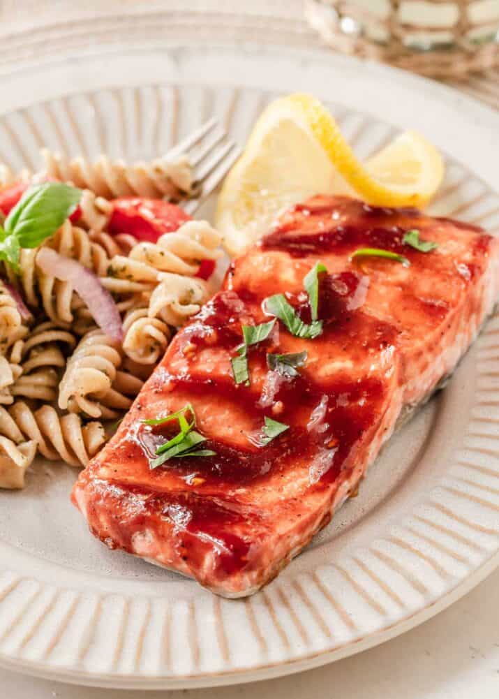 salmon with sauce brushed on, on tan plate with pasta salad.