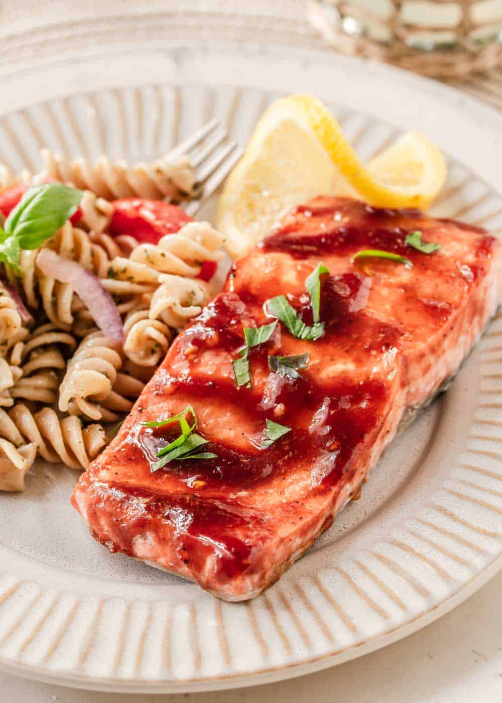 salmon with sauce brushed on, on tan plate with pasta salad.