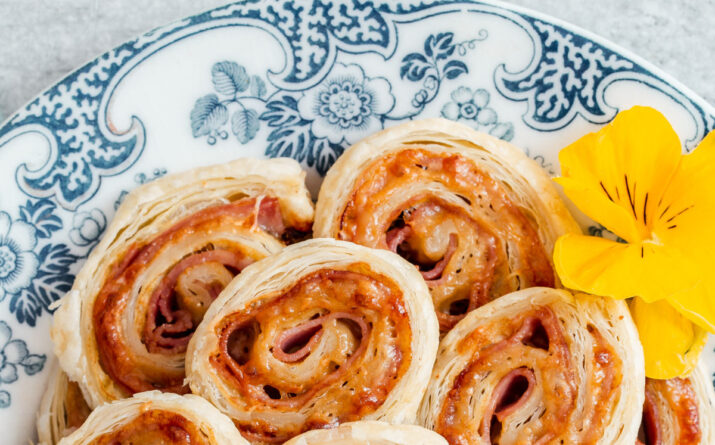 ham and cheese pinwheels pilled on to a blue and white plate with yellow flower garnish.