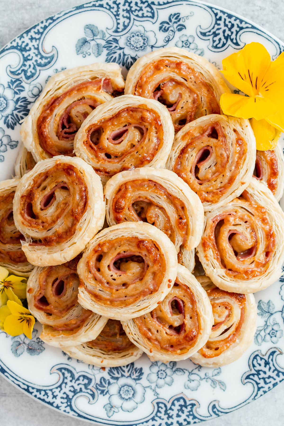 ham and cheese pinwheels pilled on to a blue and white plate with yellow flower garnish.