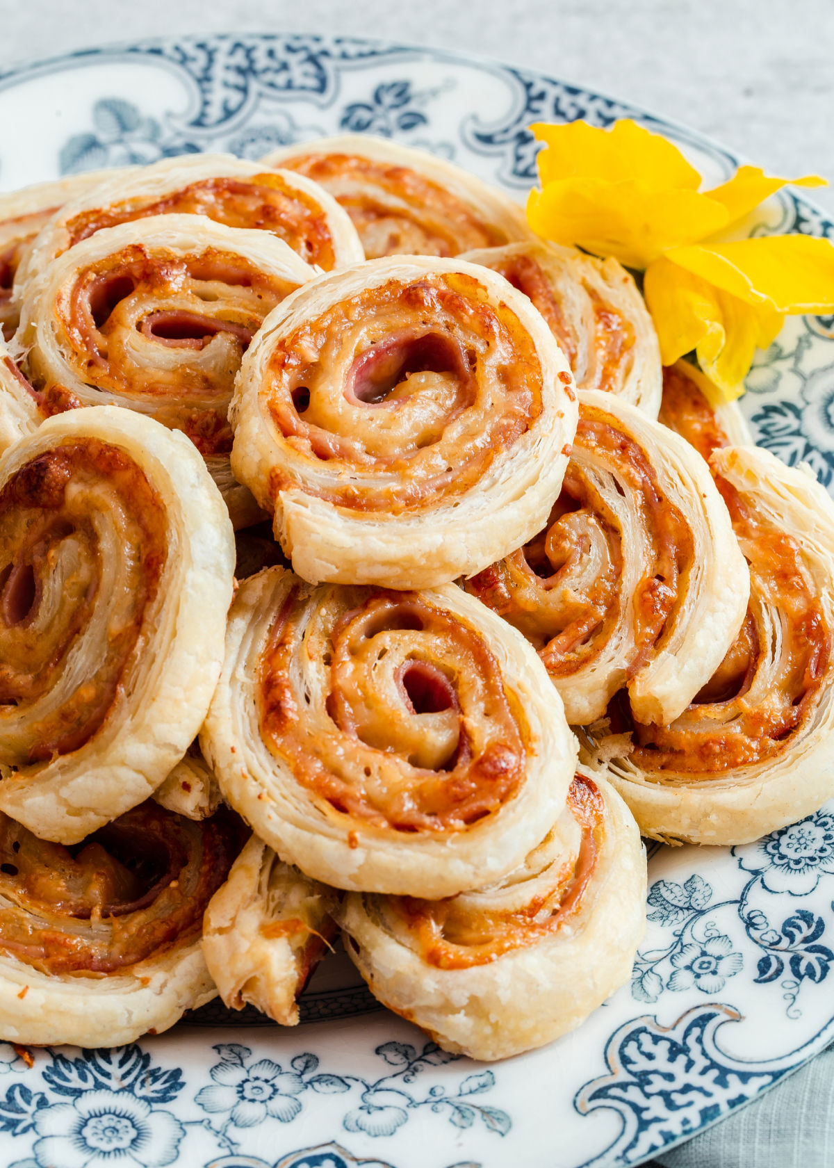 ham and cheese puff pastry pinwheel appetizers piled onto blue and white plate.