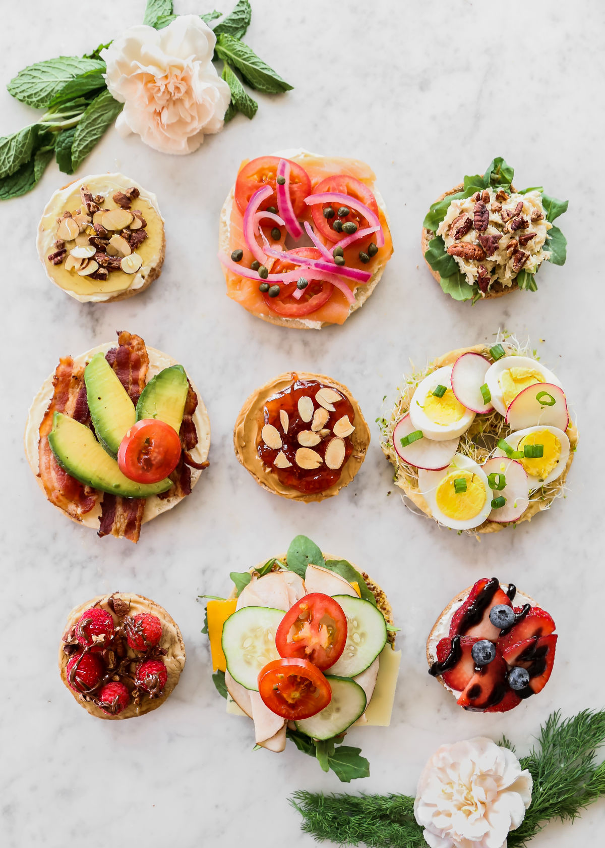 nine bagels on marble table, each topped with different toppings.