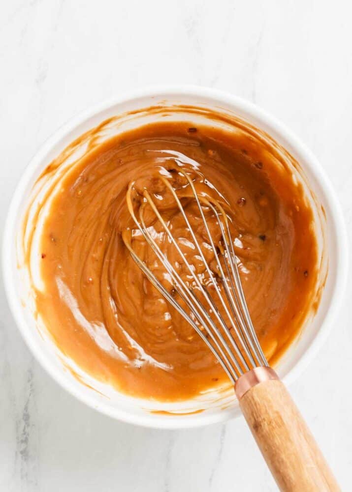 peanut dressing mixed up in white bowl with whisk.