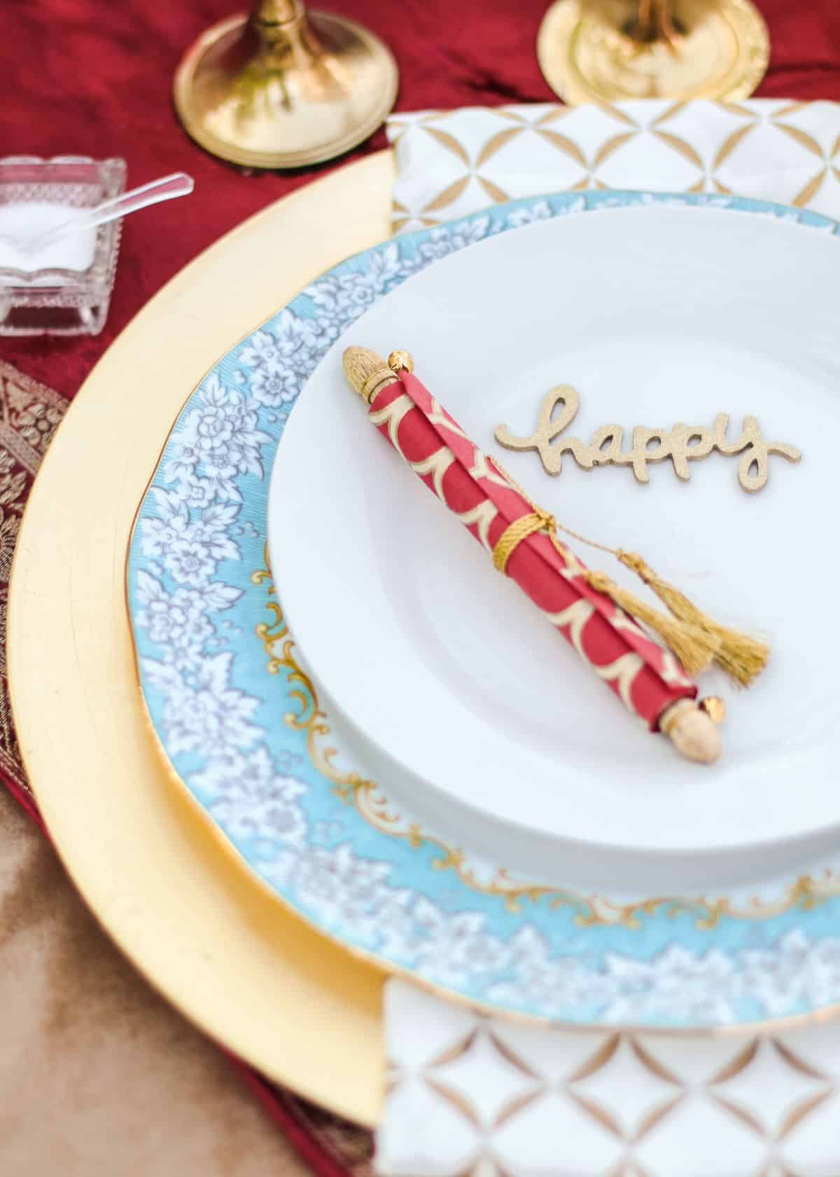 layered place setting dishes on gold charger with paper scroll on top of plate.