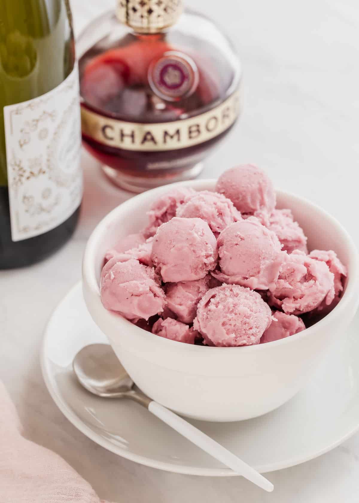mini pink sherbet scoops in small white bowl, with champagne and Chambord behind.