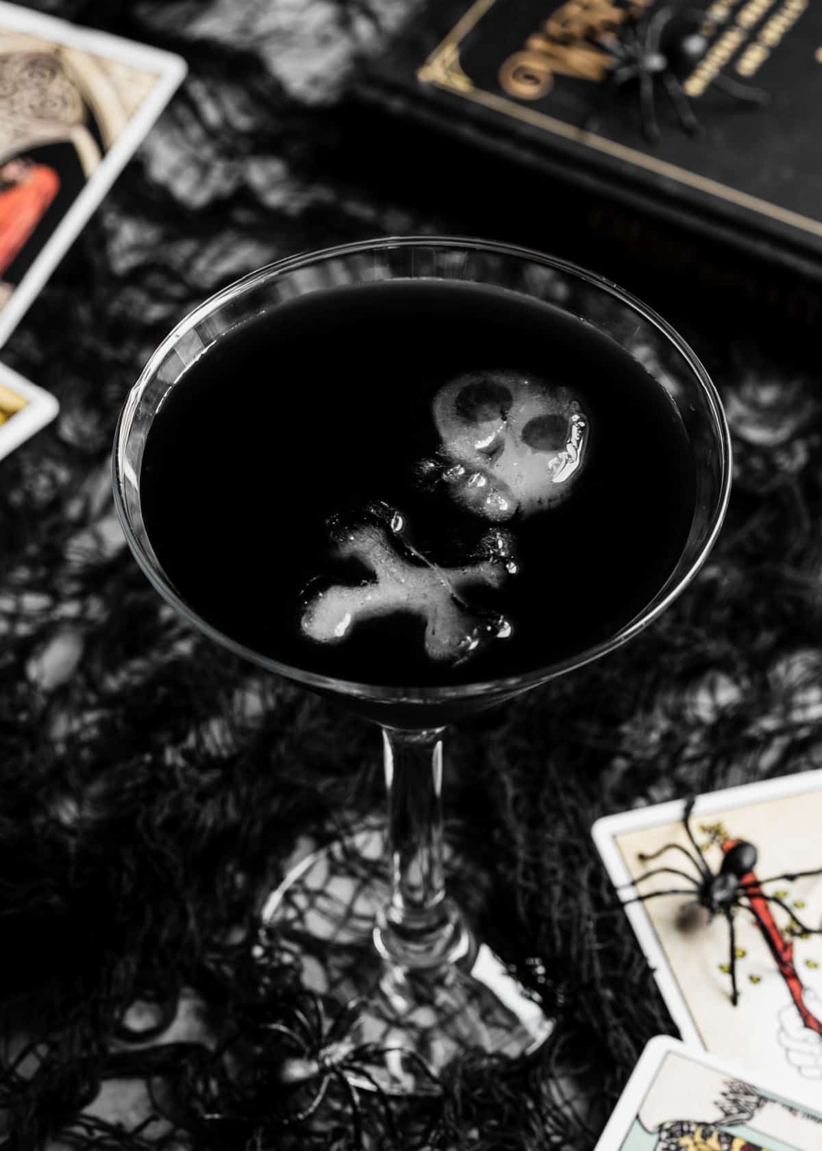 black drink in martini glass with skull and bones shaped ice.