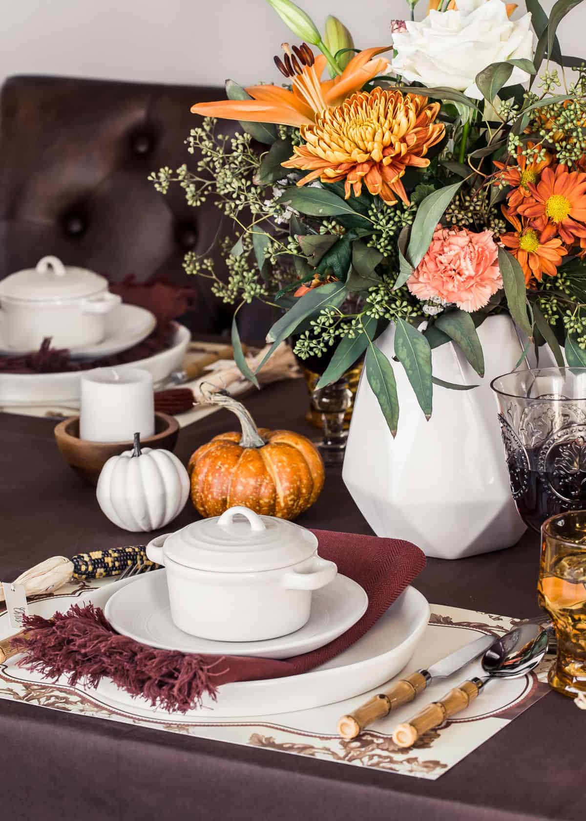 Thanksgiving table setting with brown tablecloth and white dishes, fall flower centerpiece.