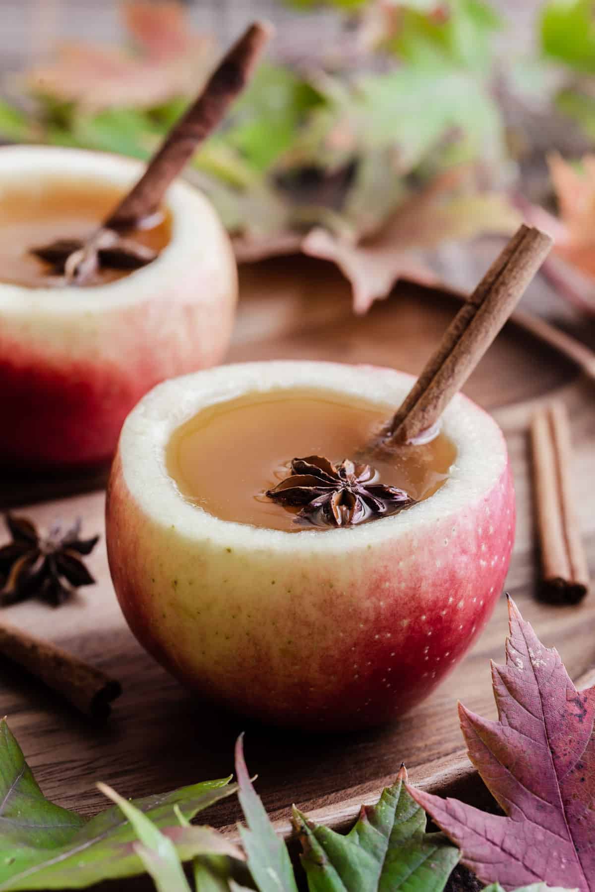 apple cider drink served in apple cups, with cinnamon stick and star anise garnish.